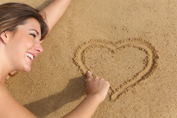 Donna felice innamorata disegnare un cuore sulla sabbia della spiaggia — Foto Stock