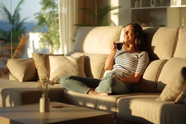 Mutlu kadın tek başına gülüyor. Gün batımında kahve içiyor. Evdeki bir kanepede oturuyor.