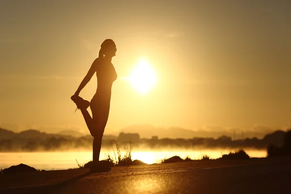 Silhouette einer Fitness-Frau, die sich bei Sonnenaufgang dehnt — Stockfoto