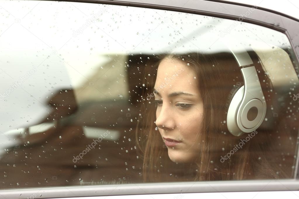 Sad teenager girl in a car with headphones