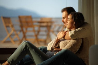 Kapalı gözlerle birbirine sarılan bir çiftin profili. Evdeki pencerenin yanında oturup rahatlarken.