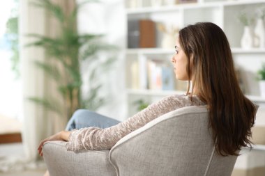 Rahatlamış bir kadın evdeki koltuktan pencereye bakıyor.