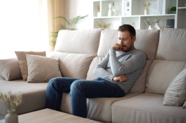 Üzgün adam evde bir kanepede tek başına oturmaktan şikayet ediyor.