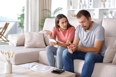 Kadın, kocasını azarlıyor. Masrafları kontrol ediyor. Evdeki kanepede oturuyor.