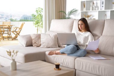 İnternette çalışan bir kadın evdeki bir kanepede oturup belgeleri kontrol ediyor.