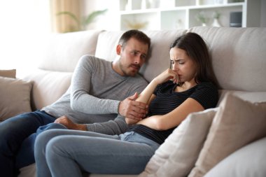 Evdeki kanepede oturan üzgün karısını teselli eden bir koca.