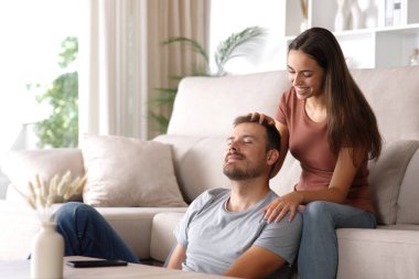 Kadın, evdeki koltukta oturan ortağına masaj yapıyor.