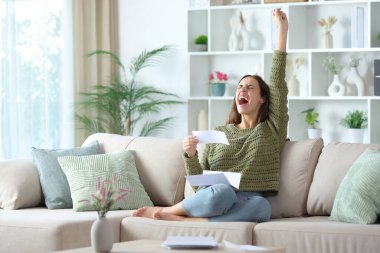 Faturayı ve mektubu evdeki kanepede oturarak kutlayan heyecanlı kadın.
