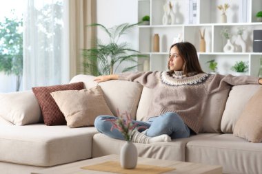 Kışın kollarını açmış rahat bir kadın evdeki kanepede oturuyor ve başka tarafa bakıyor.