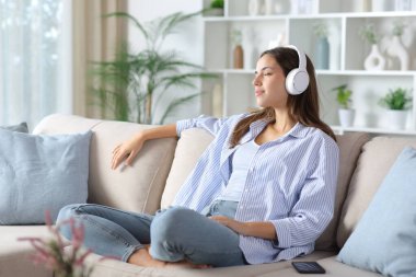 Kulaklık takan rahat bir kadın evdeki bir kanepede oturmuş ürpertici sesler dinliyor.