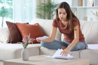 Faturaları ve banka hesaplarını kontrol eden bir kadın evdeki bir koltukta oturuyor.