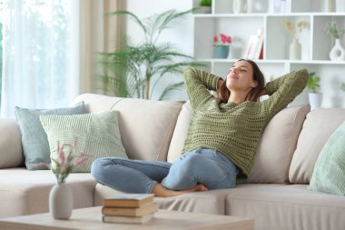 Yeşilli kadın evdeki kanepede oturuyor.