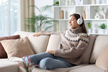 Kışın evde bir kanepede oturup kulaklıkla müzik dinlemekten zevk alan bir kadın. 