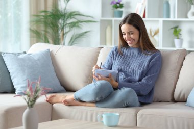 Evdeki kanepede oturan mavi elbiseli mutlu kadın deftere yazı yazıyor.