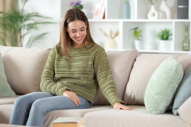 Yeşil elbiseli mutlu kadın evde yumuşak kanepe kumaşı giyiyor.