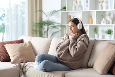 Kışın evde bir kanepede oturmuş kulaklıktan gelen sesi dinleyen bir kadın.