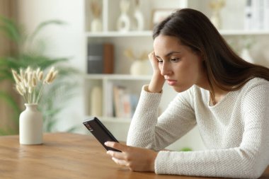 Evde bir masada oturup akıllı telefonları kontrol etmekten sıkılmış bir kadın.