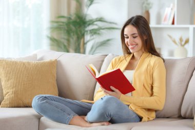 Sarı elbiseli mutlu bir kadın kırmızı kağıt okuyor. Evdeki bir kanepede oturuyor.
