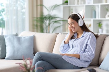 Mutlu kadın kulaklıktan komik sesler dinliyor ve evdeki kanepede oturup gülüyor.