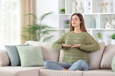 Nefes alma egzersizi yapan bir kadın evdeki koltukta oturuyor.