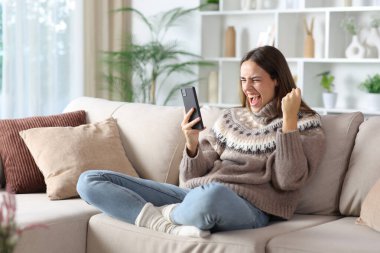 Heyecanlı kadın iyi haberi kutluyor. Kışın telefon kontrol ediyor. Evdeki bir kanepede oturuyor.