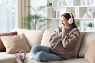 Kışın kulaklık takan mutlu bir kadın evdeki bir kanepede oturup ısınan sesleri dinliyor.