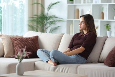 Dalgın bir kadın evdeki kanepede otururken kafasını çeviriyor.