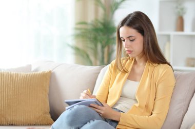 Evdeki kanepede oturan sarı elbiseli ciddi bir kadın.