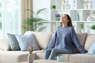 Mavili kadın temiz hava soluyor ve evdeki kanepede rahatlıyor.