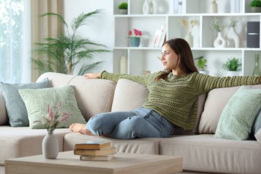 Yeşilli kadın evdeki kanepede otururken kafasını çeviriyor.