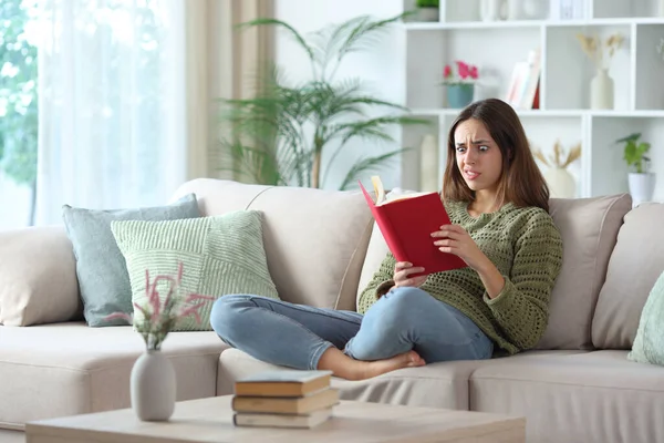 Yeşilli kafası karışmış bir kadın evde bir kanepede oturmuş kırmızı bir kitap okuyor.