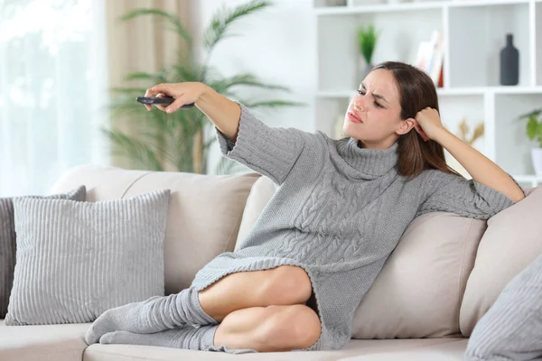 Kışın televizyon kumandası kullanan sinirli kadın evdeki kanepede oturuyor.