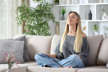 Sarışın kadın evde dinleniyor. Kanepede oturmuş temiz hava soluyor.