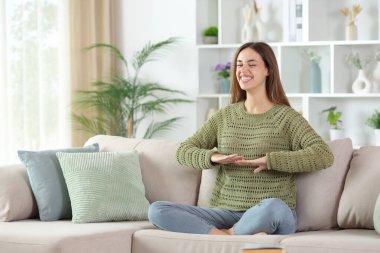 Yeşilli mutlu kadın yoga yapıyor, nefes egzersizleri yapıyor evdeki koltukta oturuyor.