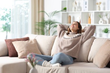 Kışın rahat ve nefes alan mutlu bir kadın evdeki kanepede oturuyor.