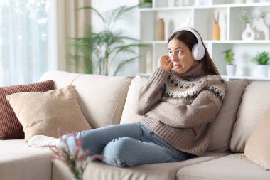 Kışın evde bir kanepede oturan kafası karışık bir kadın sesi dinliyor.