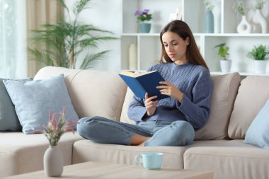 Mavili rahat kadın evdeki kanepede oturmuş gazete okuyor.