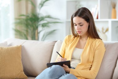 Tablette sarı el yazısı olan ciddi bir kadın evdeki kanepede oturuyor.