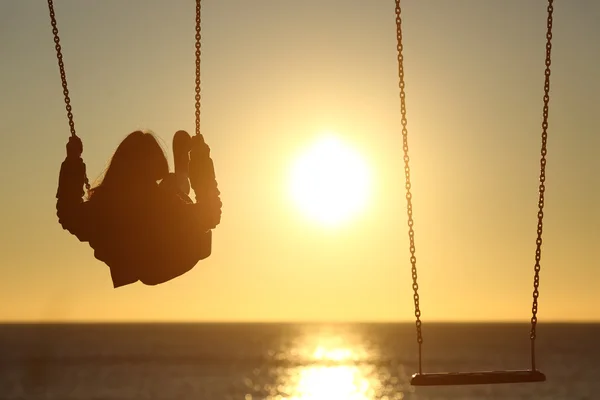 Lonely woman silhouette swinging at sunset on the beach — Stock Photo, Image