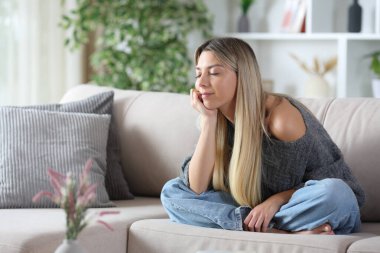 Evdeki koltukta oturan rahat sarışın kadın.