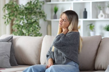 Gri boynu ağrıyan kadın evdeki kanepede oturuyor.