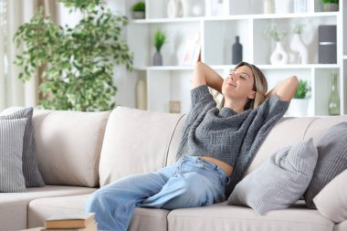 Gri elbiseli kadın evdeki kanepede dinleniyor.