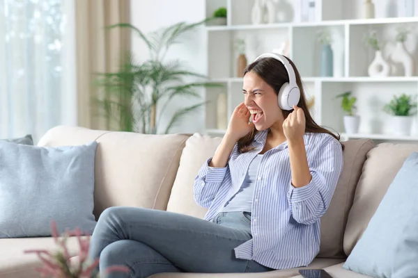 Kulaklık takmış, müzik dinleyip evdeki koltukta oturup kutlama yapan heyecanlı bir kadın.