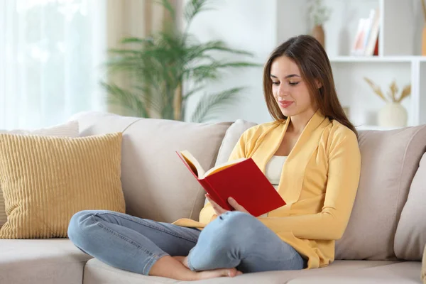 Sarılı ciddi bir kadın kırmızı kitap okuyor. Evdeki kanepede oturuyor.