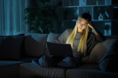 Rahat bir kadın gecenin bir yarısı evinde bir kanepede dizüstü bilgisayar kullanarak oturuyor.