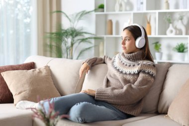 Kışın rahat bir kadın kulaklık takıyor ve evde bir kanepede oturuyor.