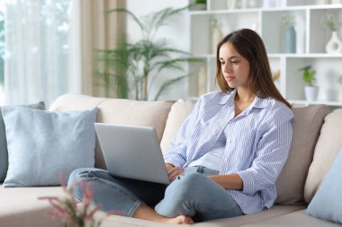 Relaxed woman in blue using laptop sitting on a sofa at home