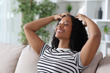 Mutlu siyahi kadın kendi kendine masaj yapıyor. Elleri evde bir koltukta oturuyor.