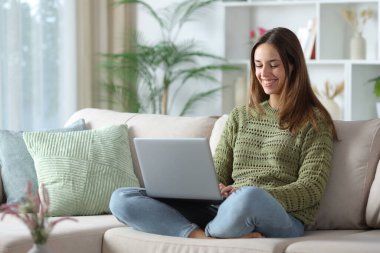 Yeşilli mutlu kadın evdeki koltukta oturan kişisel bilgisayarını kullanıyor.