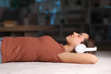 Kulaklık takan bir kadının yan görüntüsü. Evde bir halıda müzik dinleyen bir kadının.